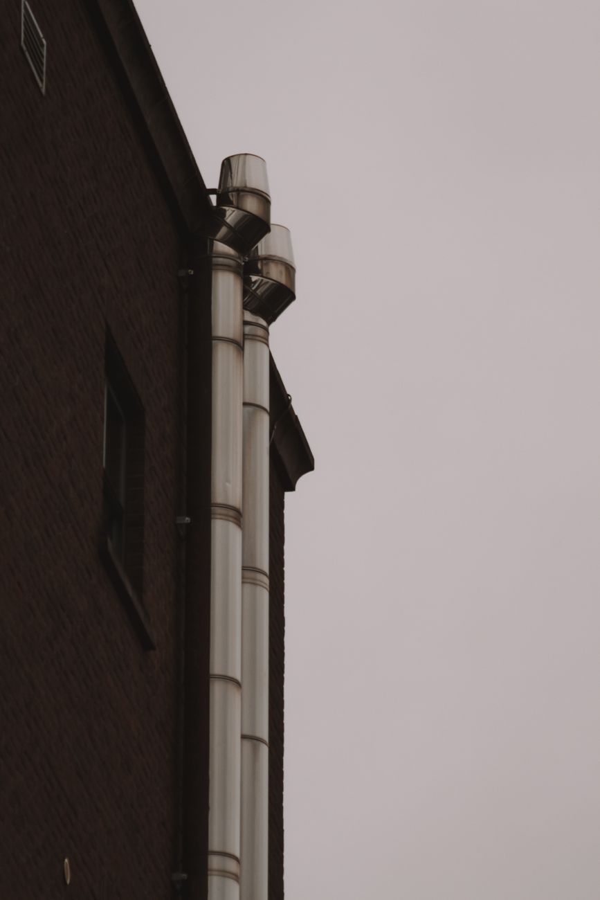 Dark brick facade with twin steel chimney flues against a pale sky